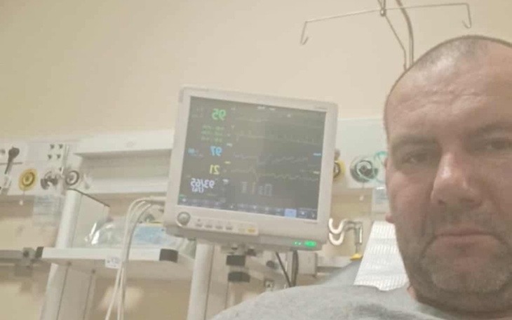 Mężczyzna w szpitalu, z monitorami medycznymi w tle, wygląda na zmartwionego.