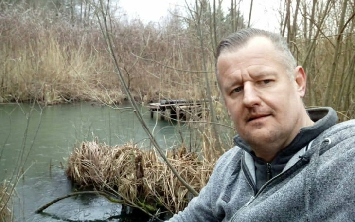 Mężczyzna siedzący nad wodą, w otoczeniu przyrody.