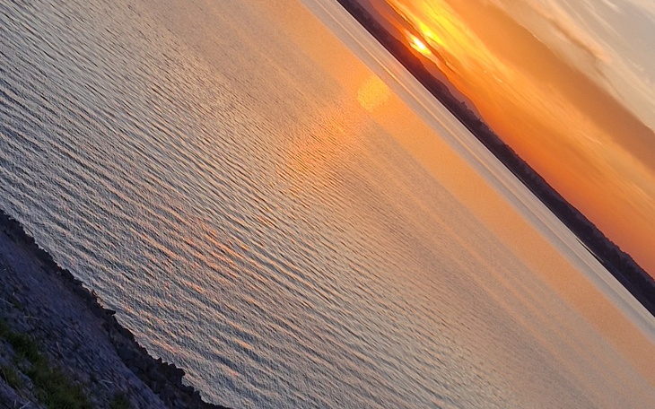 Zachód słońca nad wodą, z odbiciem w tafli.