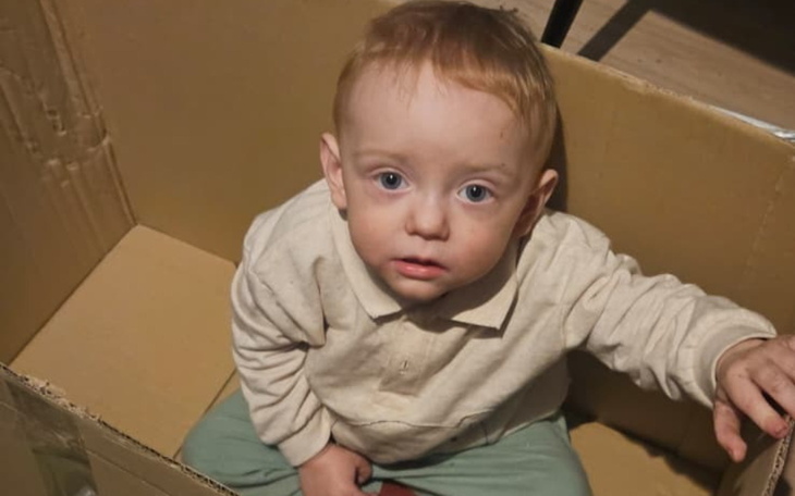 Mały chłopiec siedzący w kartonie, z zaskoczonym wyrazem twarzy.