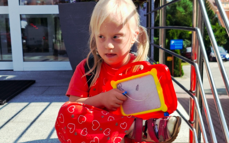 Mała dziewczynka w czerwonym stroju trzyma zabawkę i siedzi na schodach.