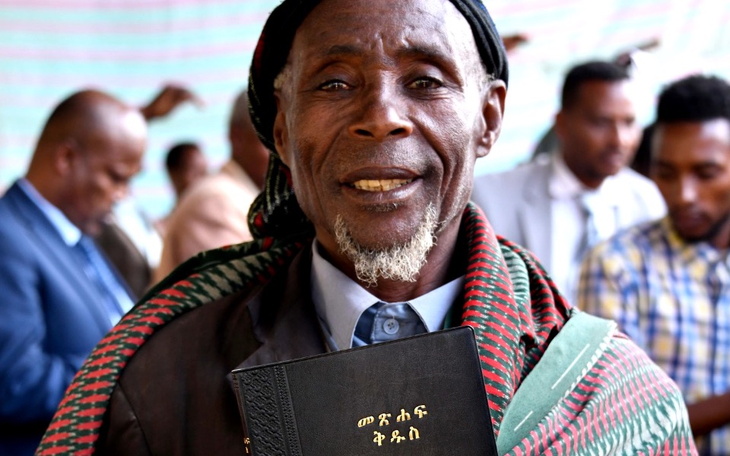 Mężczyzna trzymający książkę, uśmiechający się do kamery.