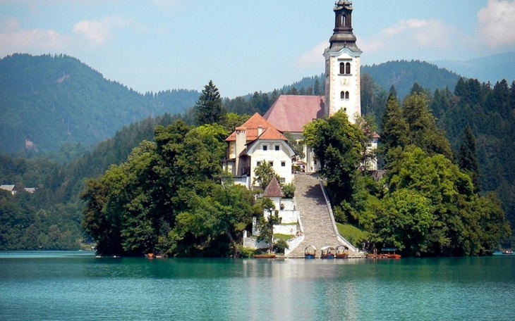Malowniczy widok na zamek na wyspie w jeziorze, otoczony górami.