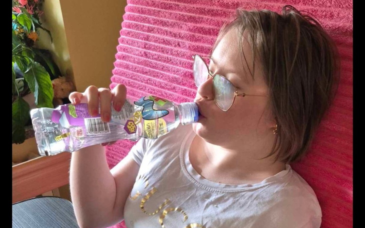 Dziewczyna pije wodę z butelki, siedząc na kanapie.