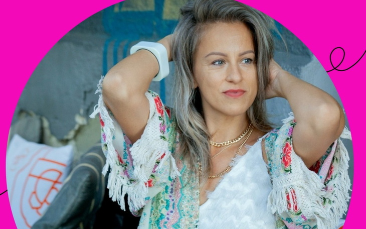 Kobieta w kolorowej bluzce, z uśmiechem na tle różowego tła.