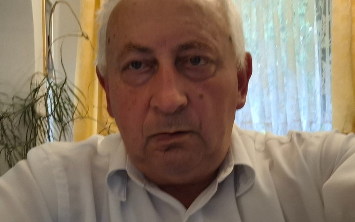 Mężczyzna w białej koszuli, z poważnym wyrazem twarzy.