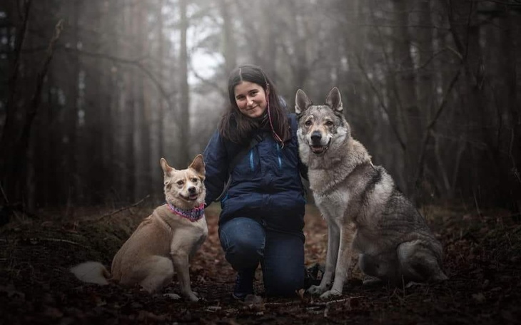 Kobieta z dwoma psami w lesie, w mglistym otoczeniu.