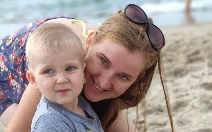 Kobieta z dzieckiem na plaży, oboje uśmiechnięci.