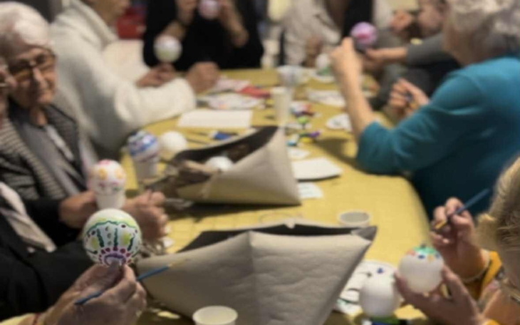 Grupa osób malujących pisanki przy stole.