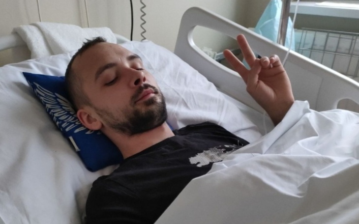 Mężczyzna w szpitalnym łóżku, pokazujący znak pokoju.