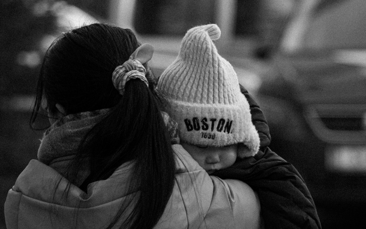 Kobieta trzymająca dziecko w czapce na ramieniu.