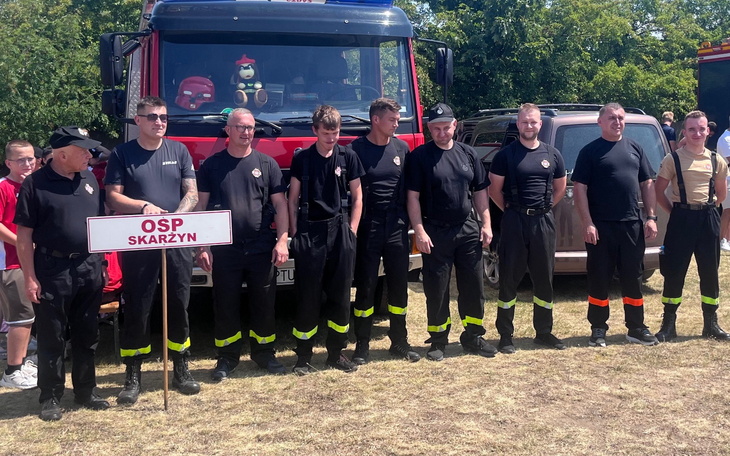 Grupa strażaków w mundurach obok wozu strażackiego.