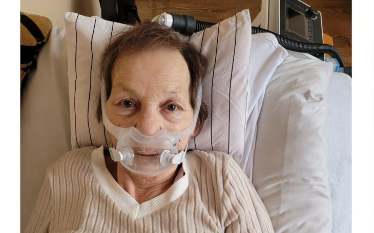 Starsza kobieta leżąca w łóżku z maską tlenową na twarzy.
