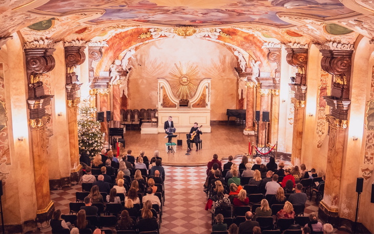 Koncert w pięknie zdobionej sali, z widownią i artystami na scenie.