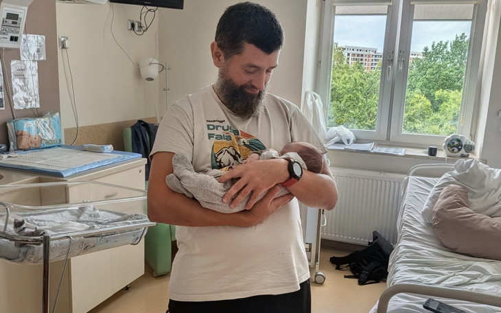 Tata tuli niemowlę w zatroskanym, ale spokojnym wyrazie, w sali szpitalnej.