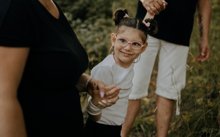 Uśmiechnięta dziewczynka trzyma się za rękę z dorosłym.
