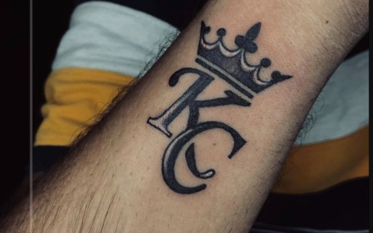 Tatuaż z literami i koroną na przedramieniu.