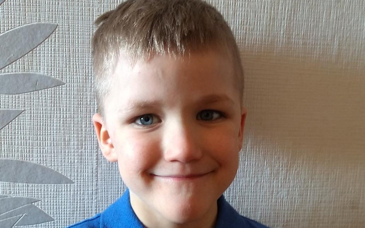 Chłopiec uśmiechający się do kamery, w niebieskiej koszulce.