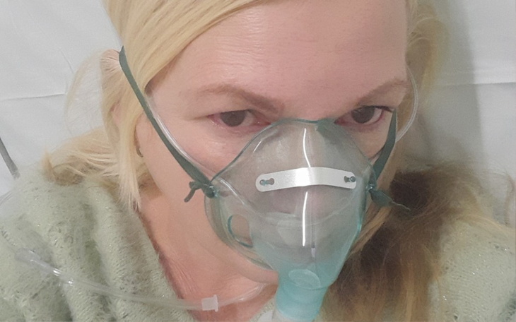 Kobieta w szpitalu z maską tlenową, wygląda na zmartwioną.