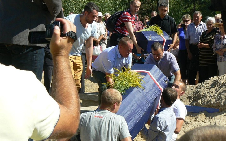 Mężczyźni niosący trumnę na pogrzebie, w tle tłum ludzi.