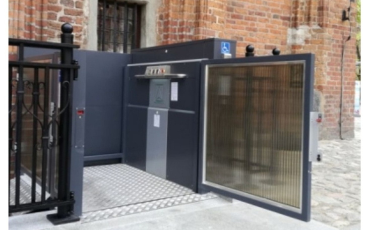 Nowoczesna winda dla osób z niepełnosprawnościami przy zabytkowym budynku.