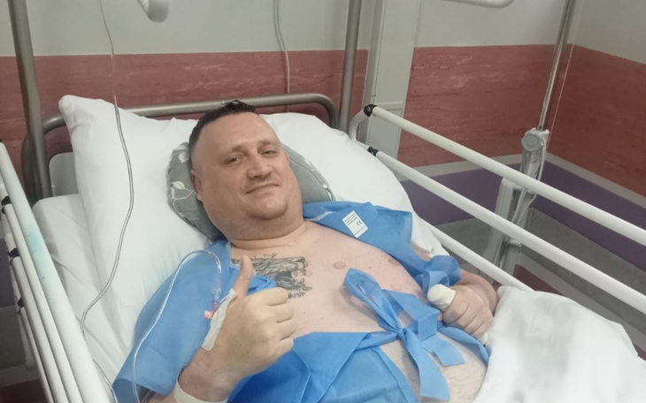 Mężczyzna w szpitalu, uśmiechający się i pokazujący kciuk w górę.