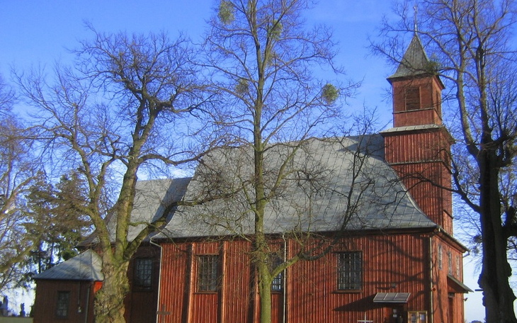 Czerwony kościół otoczony drzewami w słoneczny dzień.