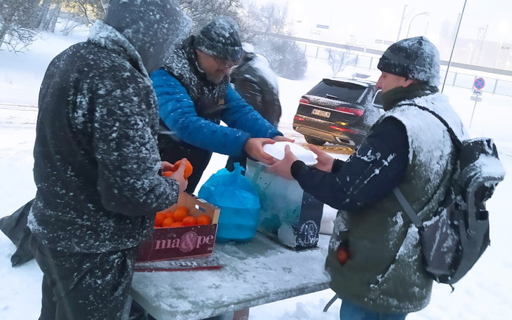 Mężczyźni w zimowych ubraniach, dzielący się jedzeniem w śniegu.