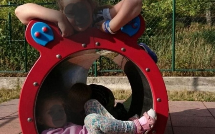 Dzieci bawiące się w kolorowej huśtawce na placu zabaw.