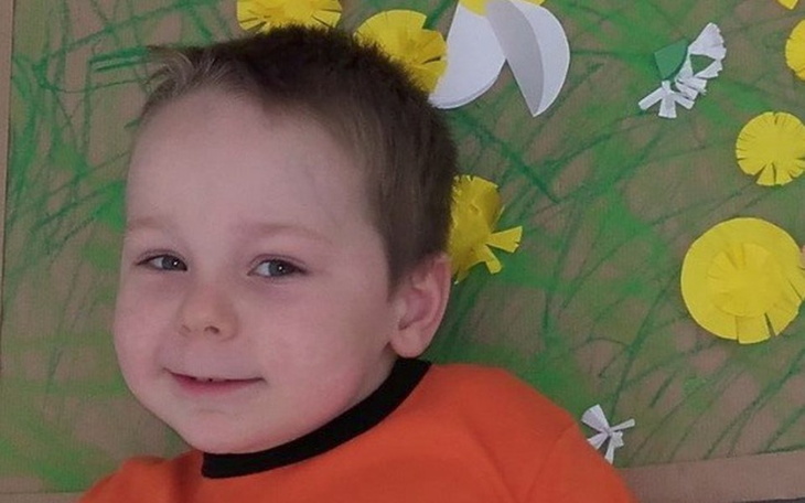 Chłopiec z uśmiechem, leżący na tle kwiatów.