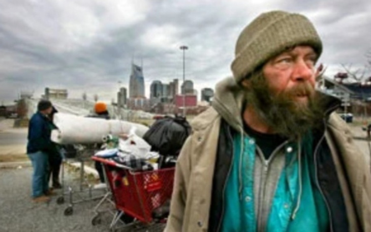 Bezdomny mężczyzna na ulicy, z wózkiem i torbami.