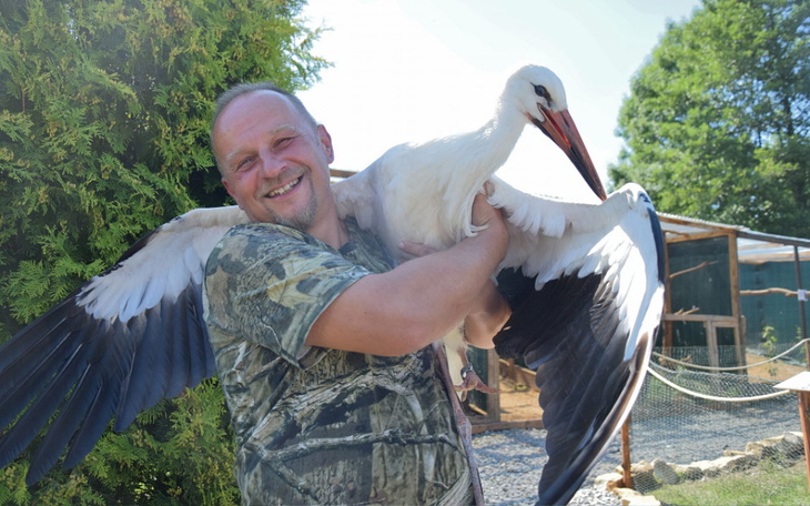 Mężczyzna trzyma bociana, uśmiechając się do kamery.