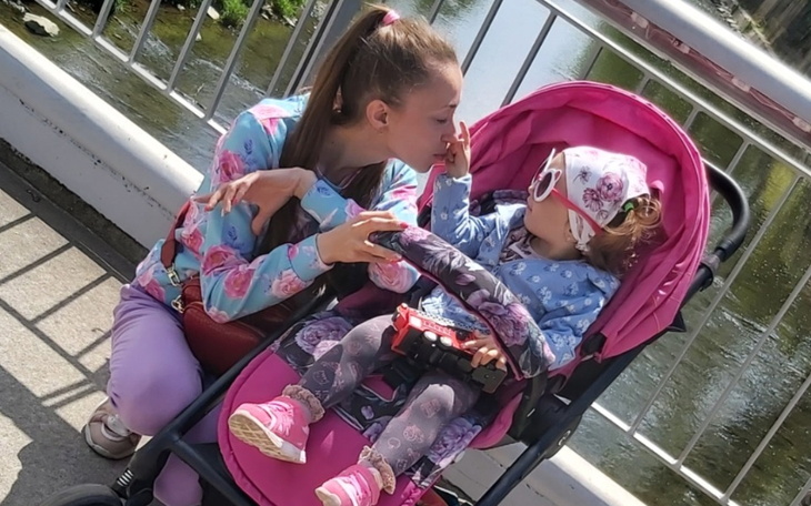 Mama całuje swoją córkę w wózku, obie uśmiechnięte.