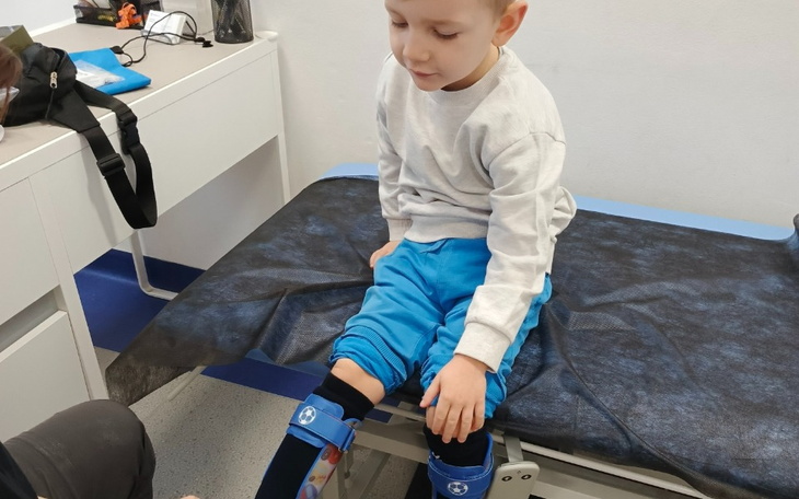 Chłopiec siedzący na łóżku, z ortopedycznymi nakolannikami.