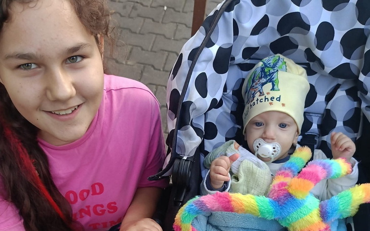 Uśmiechnięta dziewczyna z niemowlęciem w wózku, otulonym kolorowym kocykiem.