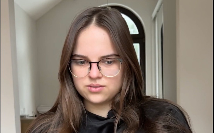 Młoda kobieta z zamyśloną miną, siedząca w jasnym pomieszczeniu.