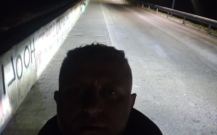 Samotna osoba na pustej drodze w nocy, oświetlona latarnią.