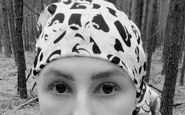 Kobieta w chustce na tle lasu, patrzy w obiektyw.