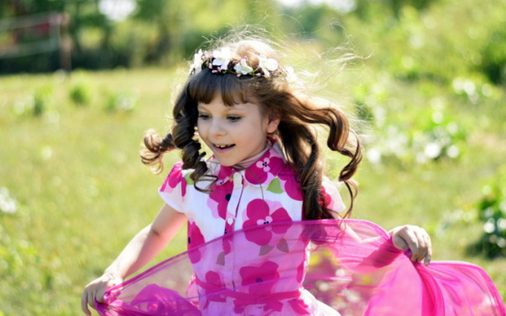 Dziewczynka w różowej sukience bawi się na łące.