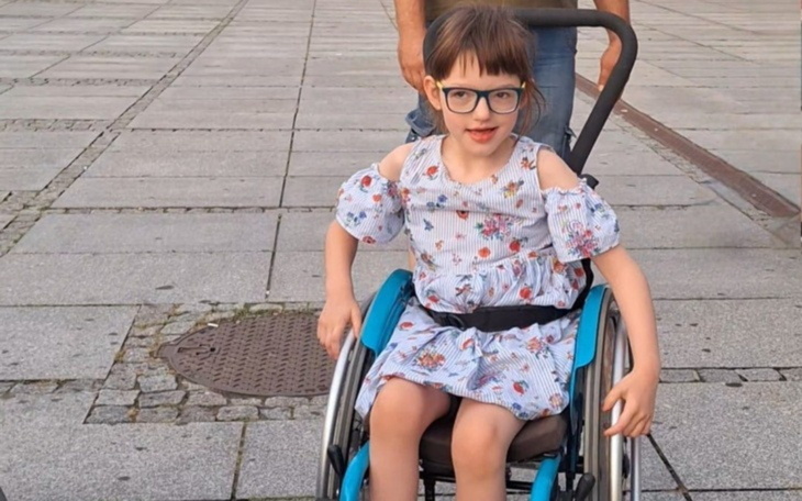 Dziewczynka w wózku inwalidzkim, uśmiechająca się do kamery.