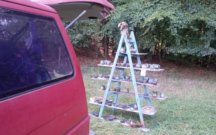 Stojak z ceramiką na tle zieleni, obok czerwony samochód.