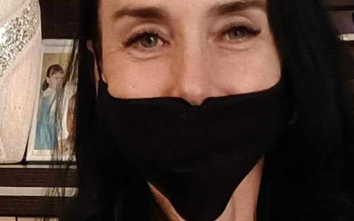 Kobieta w czarnej masce, uśmiechająca się do kamery.