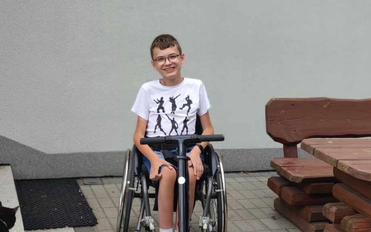 Chłopiec na wózku inwalidzkim, uśmiechający się do kamery.