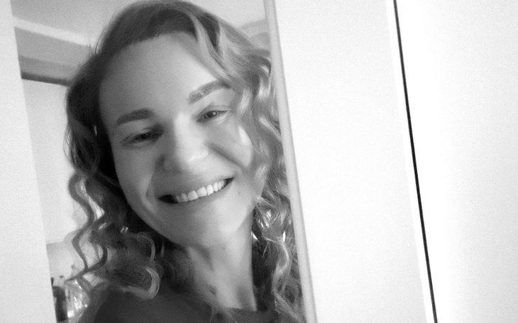 Uśmiechnięta kobieta w drzwiach, w czarno-białym ujęciu.