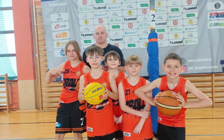 Grupa dzieci w strojach sportowych na boisku do koszykówki.