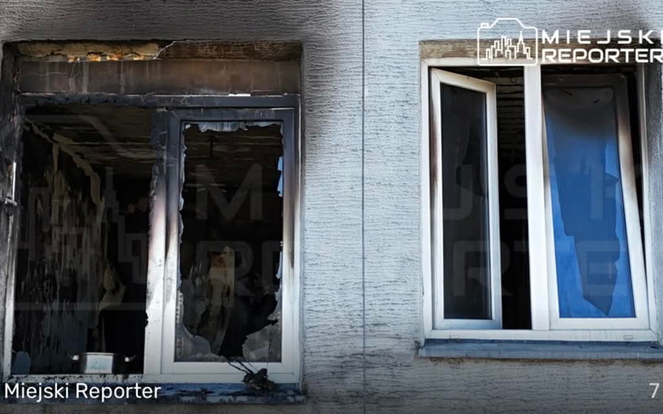 Zniszczone okna budynku po pożarze, widoczne uszkodzenia.