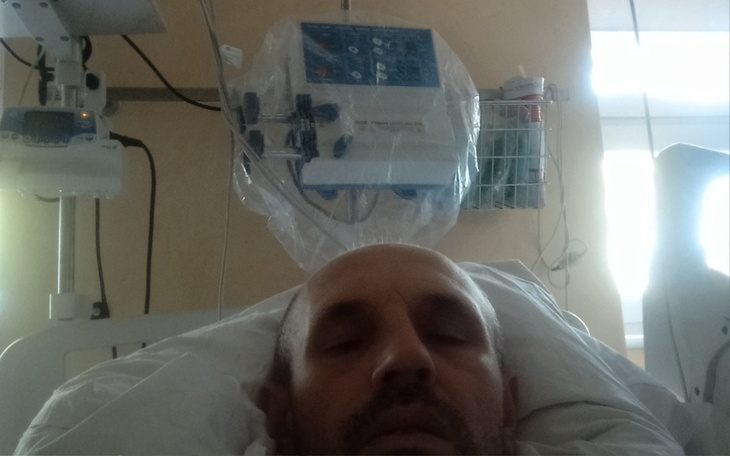 Mężczyzna leżący w szpitalnym łóżku, z widocznym sprzętem medycznym.