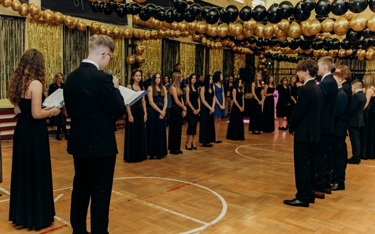 Uroczystość w eleganckiej sali, z gośćmi w strojach wieczorowych.