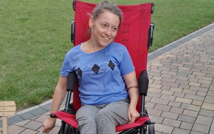 Kobieta w wózku, uśmiechająca się na świeżym powietrzu.