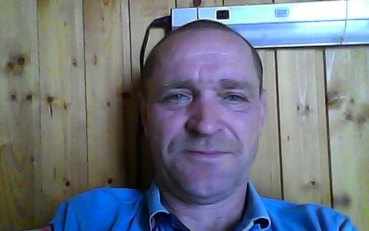 Mężczyzna z uśmiechem, siedzący w drewnianym pomieszczeniu.